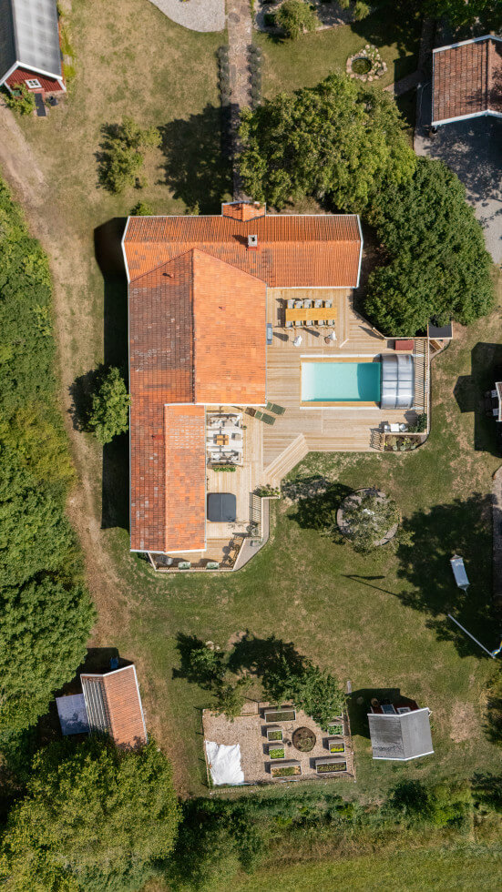 bild ovanifrån på ett hus med stort trädäck och pool.