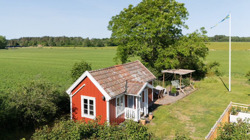 Bild på ett det ena röda gästhuset på tomten. Bakgrunden är en slätt.  