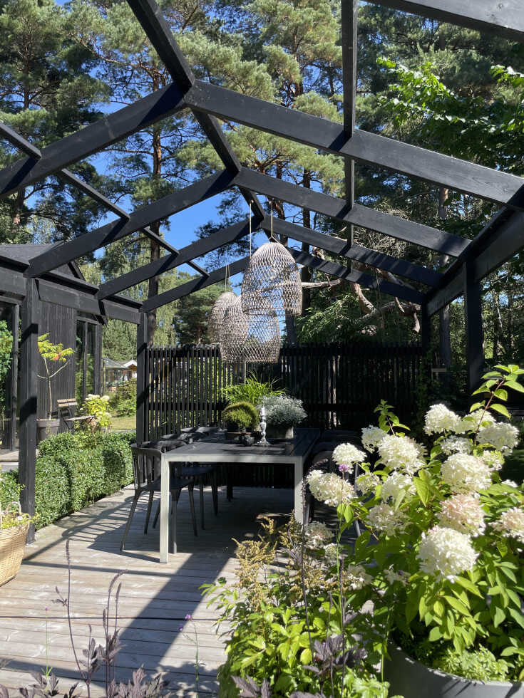 Bild på en pergola med matplats under och blommor framför.