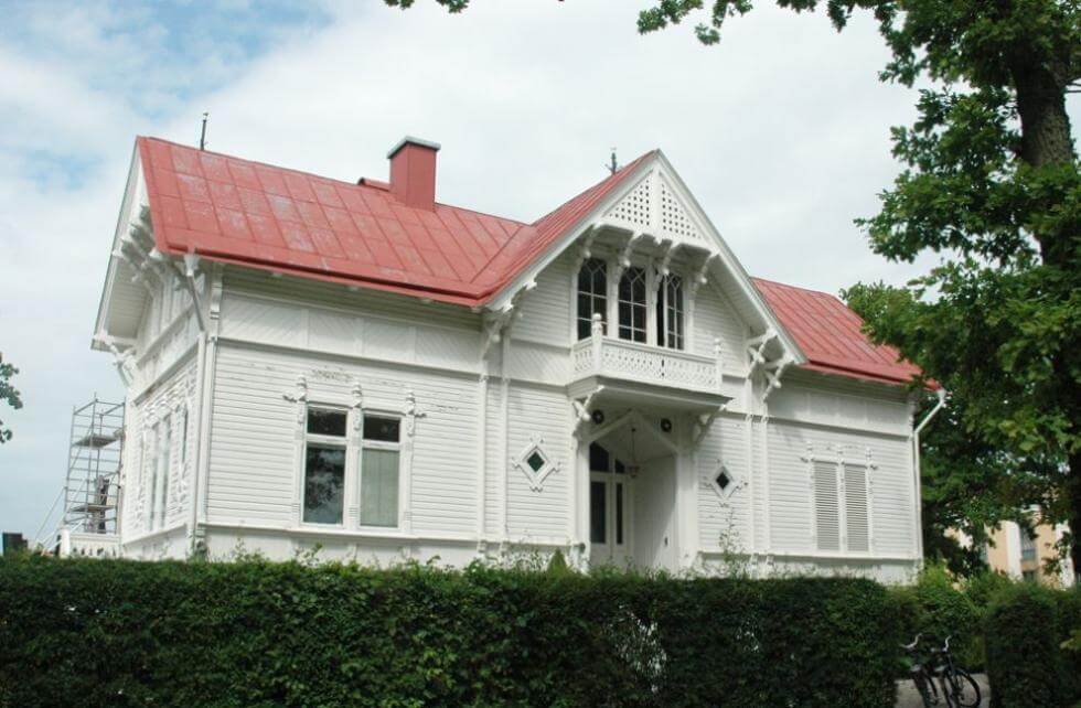 Tidsenligt färgade plåtarbeten, med hängrännor i tegelröd och stuprör i fasadens vita färg.