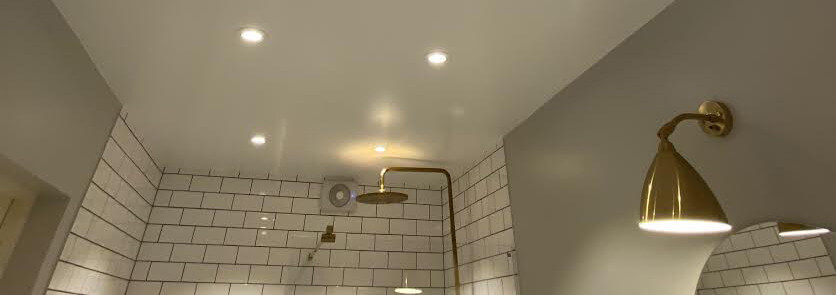 Här sitter en spotlight placerad i duschen, rakt över takduschen i mässing, vilket gör att gult ljus reflekteras i taket - inte att rekommendera enligt experterna.